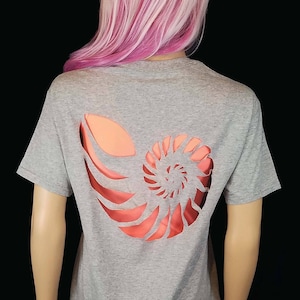 May include: A gray t-shirt with a cutout design of a nautilus shell on the back. The shell is a light orange color.
