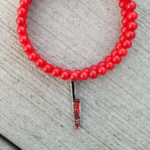 May include: Red beaded bracelet with a silver knife charm. The knife is red and black and has a serrated edge.