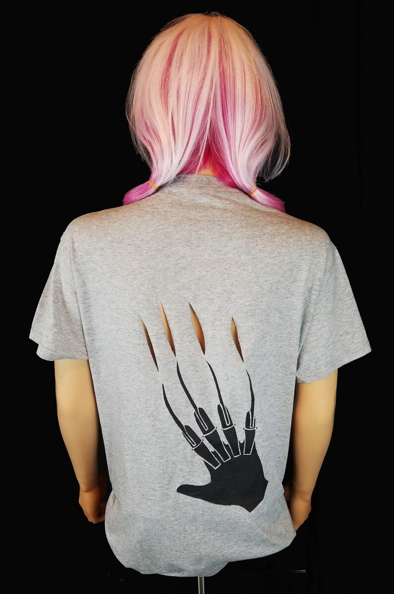 May include: Gray t-shirt featuring a black claw design on the back. The claw design has long, sharp fingernails. The shirt is made of a soft material and has short sleeves. The background is black.