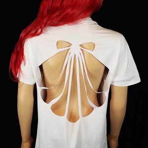May include: A white t-shirt with a large seashell cut-out on the back. The shirt is loose fitting and has short sleeves.