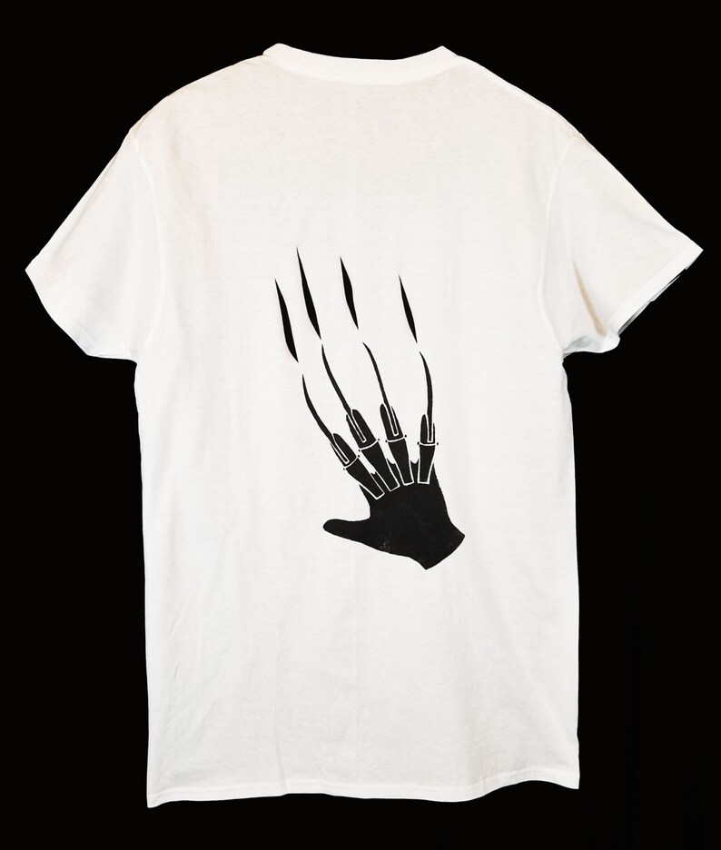 May include: White t-shirt featuring a black graphic of a hand with long, sharp claws. The clawed hand design is printed on the back of the shirt. The shirt is made of a soft, lightweight material.