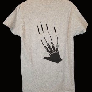 May include: A gray t-shirt with a black graphic of a hand with long claws on the back.