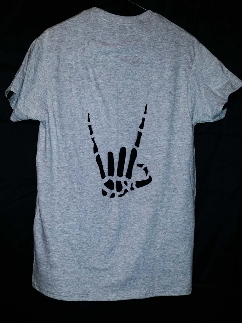Może przedstawiać: Szary T-shirt z czarnym szkieletowym ręką wykonującą gest rock and roll.