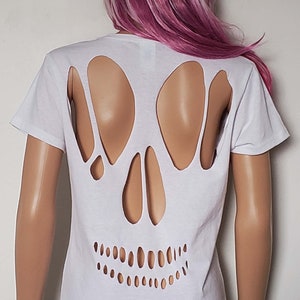 May include: White t-shirt with a skull cut-out design on the back. The skull is formed by holes in the fabric, revealing the skin underneath.