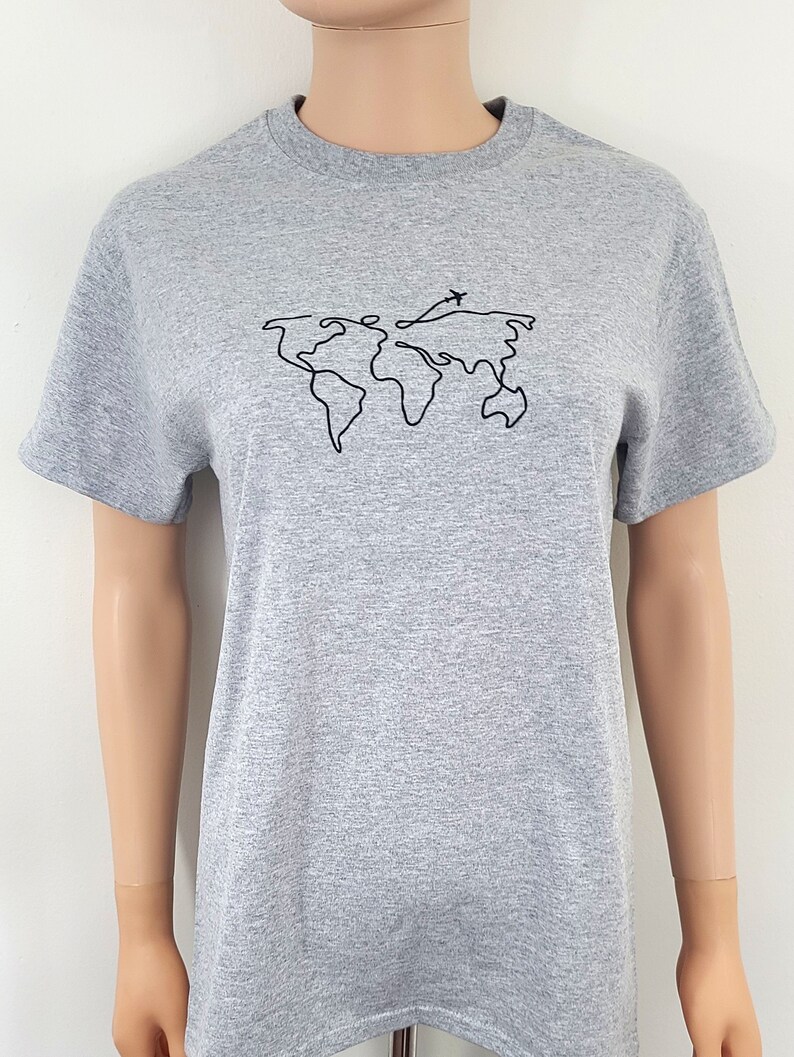K&ouml;nnte beinhalten: Ein graues T-Shirt mit einer schwarzen Linienzeichnung der Welt mit einem kleinen Flugzeug, das dar&uuml;ber fliegt.