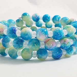 May include: A multi-strand bracelet made of blue, green, and white beads. The beads are round and have a marbled or swirled pattern.