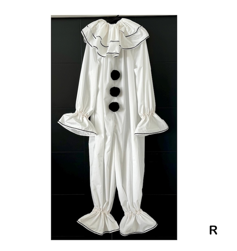 May include: A white clown costume with a ruffled collar and cuffs, accented with black trim. The one-piece outfit features three large black pom-poms down the front and flared sleeves and pant legs.