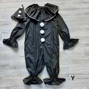 May include: Black clown costume with a ruffled collar and cuffs, and white pom-poms. The costume includes a matching hat with white pom-poms. The outfit is made of a shiny material and is designed for a playful look.