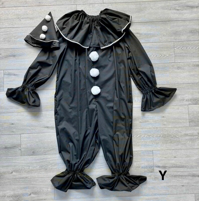 May include: Black clown costume with a ruffled collar and cuffs, and white pom-poms. The costume includes a matching hat with white pom-poms. The outfit is made of a shiny material and is designed for a playful look.