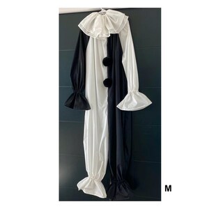 May include: A black and white clown costume with a large ruffled collar, long sleeves, and three black pom-poms down the front. The costume has flared sleeves and pant cuffs. The letter "M" is visible in the bottom right corner.