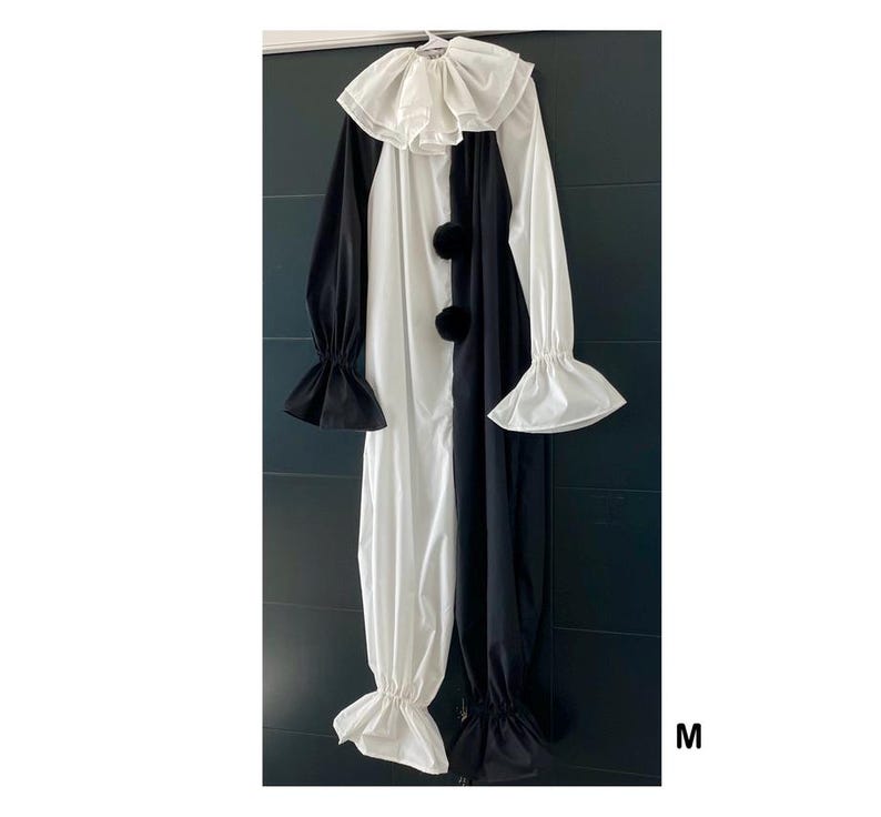 May include: A black and white clown costume with a large ruffled collar, long sleeves, and three black pom-poms down the front. The costume has flared sleeves and pant cuffs. The letter "M" is visible in the bottom right corner.
