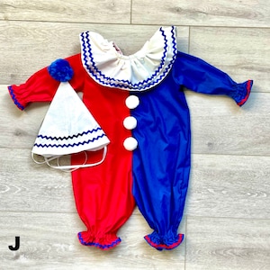 May include: A red and blue clown costume with a matching hat. The one-piece outfit has a white ruffled collar and three white pom-pom buttons. The hat is white with a blue zig-zag trim and a blue pom-pom.