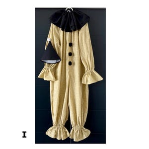May include: A full-body clown costume in a light tan fabric with a subtle pattern. The costume features a black ruffled collar, three black buttons, and ruffled cuffs and ankles. A matching black cone hat with a white pom-pom is included.
