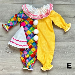 May include: A colorful clown costume with a white ruffled collar and matching hat. The costume features a harlequin pattern on one side and yellow stripes on the other. White pom-poms and pink trim add playful details to this festive outfit.