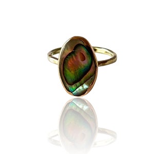 May include: A gold ring featuring an oval abalone shell inlay. The shell displays iridescent green, blue, and pink hues.