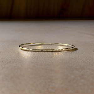 May include: A simple gold bangle bracelet with a hammered texture.