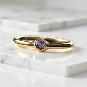 May include: A delicate gold band ring with a small, round, light purple gemstone set in the centre.