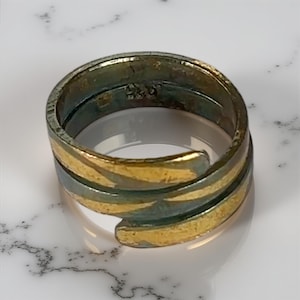 May include: A gold and green metal ring with a textured surface. The ring is open on one side and has a unique design.