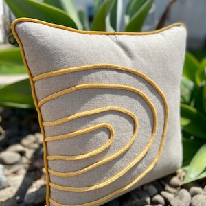 Peut inclure: Un coussin gris avec un motif de corde jaune. Le coussin est fait d'un tissu doux et texturé et a une bordure jaune.