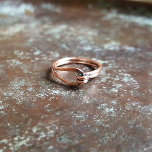 Könnte beinhalten: Ein einfacher Kupferring mit einem gedrehten Knotendesign. Der Ring besteht aus zwei Bändern aus Kupferdraht, die miteinander verdreht sind, um einen Knoten zu bilden.