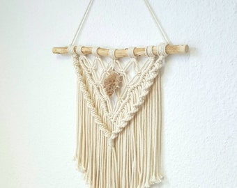 Peut inclure: Une suspension murale en macramé avec une baguette en bois naturel et un cordon en coton beige. La suspension présente un motif géométrique avec une petite coquille au centre.