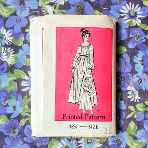 May include: A vintage dressmaking pattern with a pink panel showing illustrations of a woman and girl in the dress design. The pattern is labelled "4851 - SIZE 12". The background is a floral fabric with blue and purple flowers.