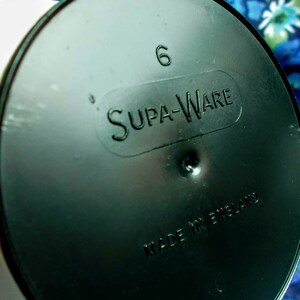 May include: A black plastic lid with the embossed text "Supa-Ware" and the number "6". The words "Made in England" are also embossed on the lid. The lid is circular and has a slightly reflective surface.
