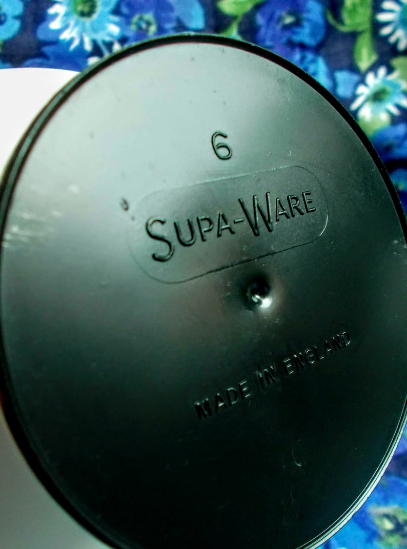 May include: A black plastic lid with the embossed text "Supa-Ware" and the number "6". The words "Made in England" are also embossed on the lid. The lid is circular and has a slightly reflective surface.