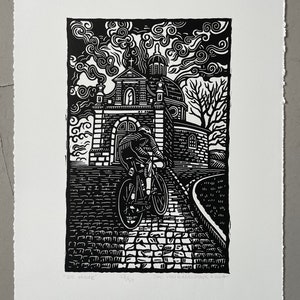 Op de afbeelding: Zwart-witte houtsnede van een fietser die een geplaveide weg opfietst naar een kerk met een koepel. De prent is getiteld "De Muur" en is genummerd 27/50. De naam van de kunstenaar en de datum zijn ook in de prent opgenomen.