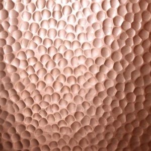 May include: A metallic copper surface featuring a dense, repeating pattern of small, concave circular indentations. The hammered texture creates a play of light and shadow across the warm, reddish-brown surface, resulting in a uniform, dimpled appearance.