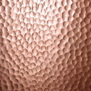 May include: A metallic copper surface featuring a dense, repeating pattern of small, concave circular indentations. The hammered texture creates a play of light and shadow across the warm, reddish-brown surface, resulting in a uniform, dimpled appearance.