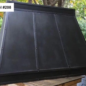 May include: Black metal range hood with a rectangular shape and a slightly angled top. The hood has a simple design with a smooth surface and a black finish. The hood is labeled "Model #208".