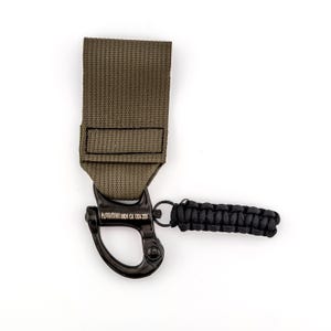 May include: A green nylon strap with a black metal hook and a black paracord lanyard. The hook is engraved with "AUTOIRONS CA USA 200".