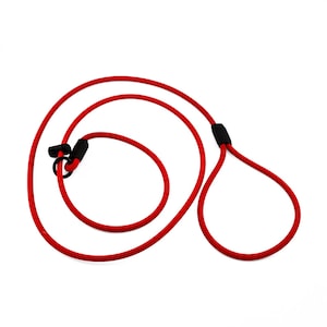 May include: A red dog leash with a loop handle and a loop for the dog's neck. The leash is made of a thick, durable rope-like material. The leash has black plastic connectors and a black plastic piece where the handle is formed.