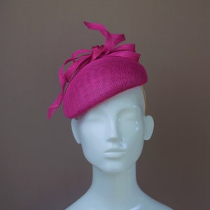 May include: A bright pink hat with a large bow on top. The hat is made of a soft, textured material and is perfect for a special occasion.