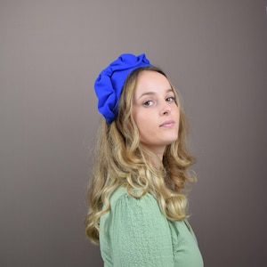 以下が含まれることがあります： 長いブロンドの髪をした女性が、明るい青色のヘッドバンドをしています。ヘッドバンドは布製で、ギャザーが寄せられ、フリルのような形をしています。女性は薄い緑色のシャツを着ています。