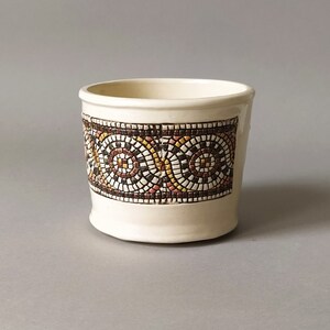 Puede incluir: Taza de cerámica blanca con un patrón de mosaico en marrón, amarillo y rojo. El patrón es un diseño repetitivo de círculos.