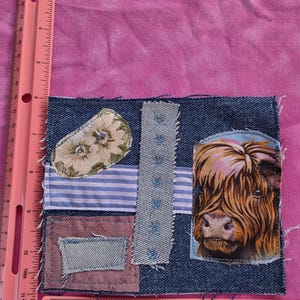 May include: A square denim fabric patch featuring a Highland cow graphic, a floral fabric piece, a blue and white striped fabric strip, and a light blue denim rectangle. A pink Westcott ruler shows the patch is 5 inches wide and 5 inches tall.