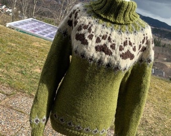 May include: A green turtleneck sweater with a white and brown patterned design featuring paw prints. The sweater is knitted and has a ribbed collar.