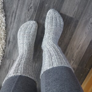 May include: A pair of gray knitted socks with a ribbed texture. The socks are folded down at the top, revealing a gray fabric underneath.