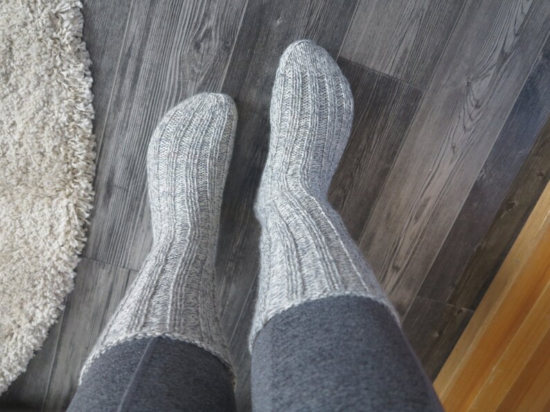 May include: A pair of gray knitted socks with a ribbed texture. The socks are folded down at the top, revealing a gray fabric underneath.