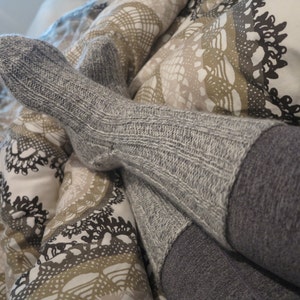 May include: A pair of gray knitted socks with a ribbed texture. The socks are worn and the top of the socks are folded down.