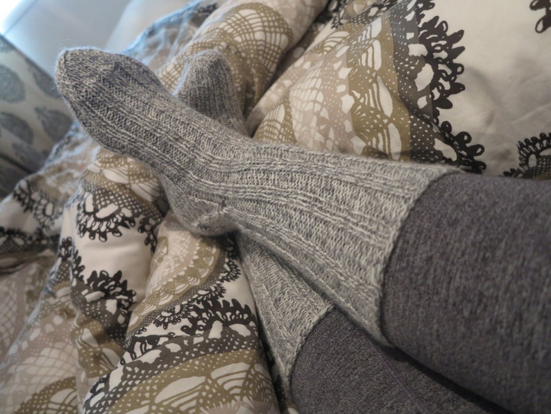 May include: A pair of gray knitted socks with a ribbed texture. The socks are worn and the top of the socks are folded down.