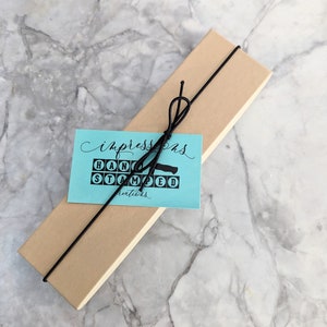 May include: A brown cardboard box with a black ribbon tied around it. A blue tag with white text reads "Impressions Hand Stamped Creations".