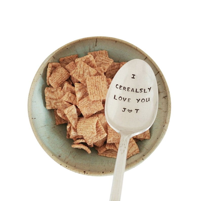 K&ouml;nnte beinhalten: Ein silberner L&ouml;ffel mit der Gravur "I Cerealsly Love You J&hearts;T". Der L&ouml;ffel liegt in einer Sch&uuml;ssel mit M&uuml;sli.