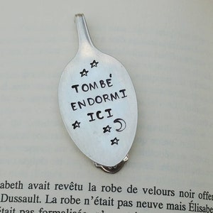 May include: A silver spoon bookmark with the words "TOMBE ENDORMI ICI" engraved on it. The spoon has a star design and a crescent moon.