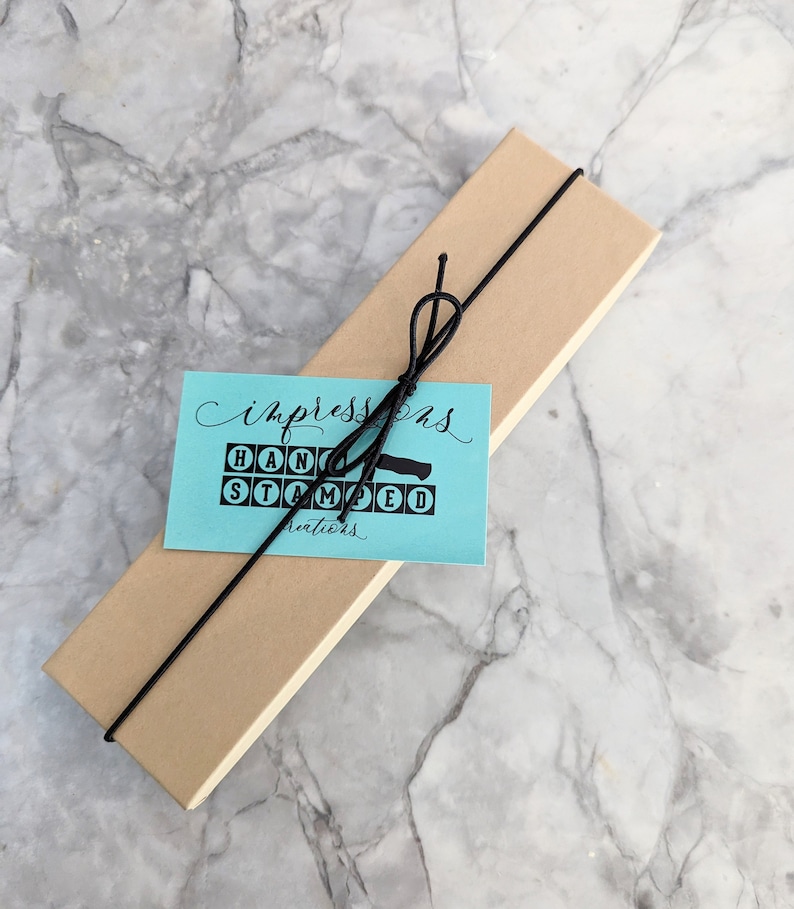 May include: A brown cardboard box with a black ribbon tied around it. A blue tag with white text reads "Impressions Hand Stamped Creations".