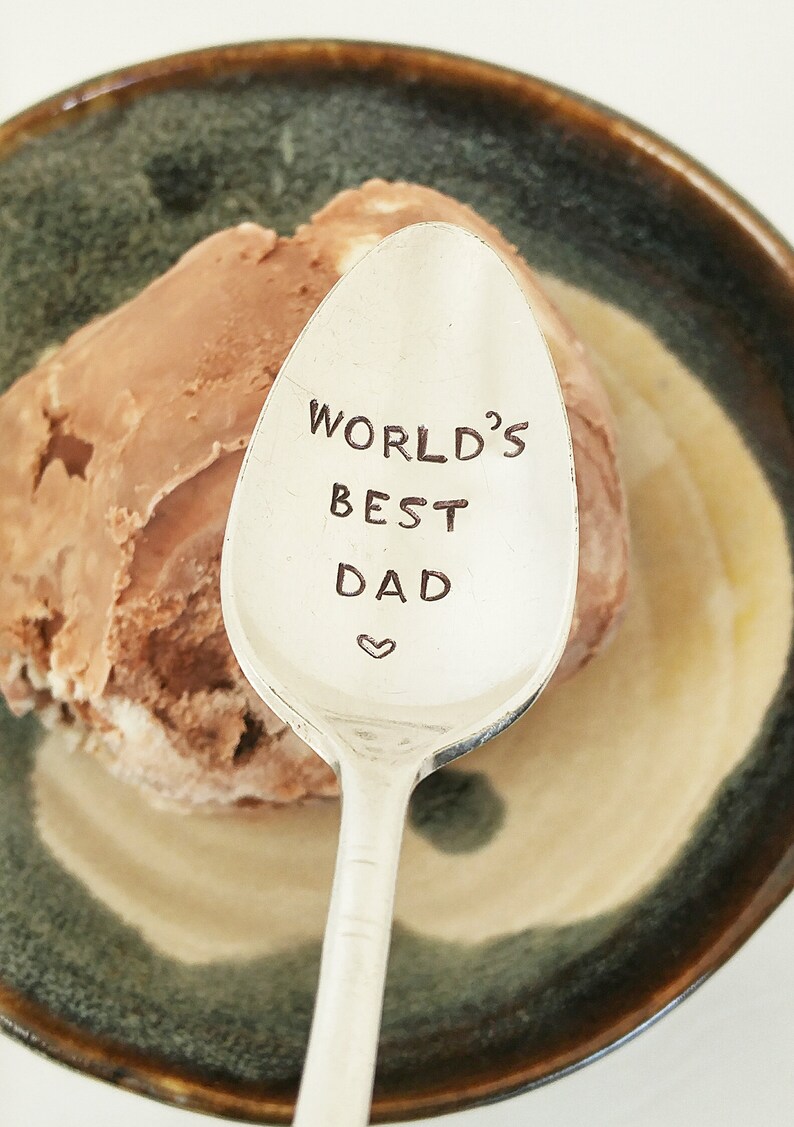 May include: A silver spoon with the words "World's Best Dad" engraved on it. The spoon is resting on a bowl of chocolate ice cream.