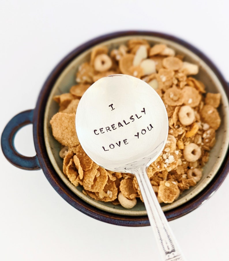 K&ouml;nnte beinhalten: Ein silberner L&ouml;ffel mit der Gravur "I Cerealsly Love You" auf der Schale. Der L&ouml;ffel liegt in einer Sch&uuml;ssel mit M&uuml;sli.