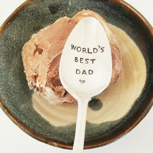May include: A silver spoon with the words "World's Best Dad" engraved on it. The spoon is resting on top of a scoop of chocolate ice cream in a brown and green bowl.